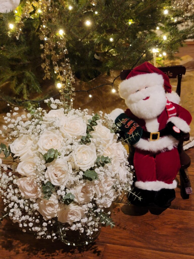 A stuffed santa claus sitting next to a bouquet of white roses