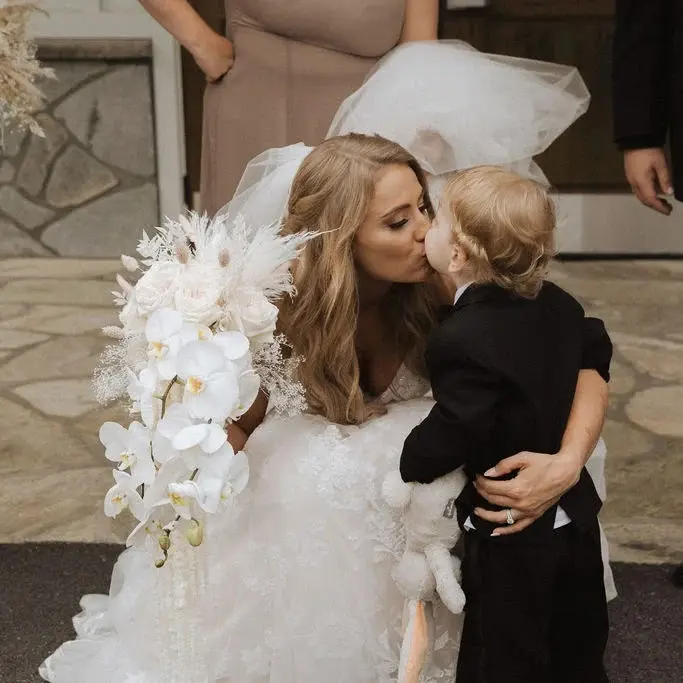 A woman in a wedding dress kisses a little boy on the cheek