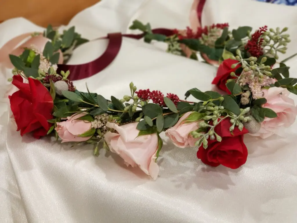 A flower crown made of red and pink roses is sitting on a white cloth.