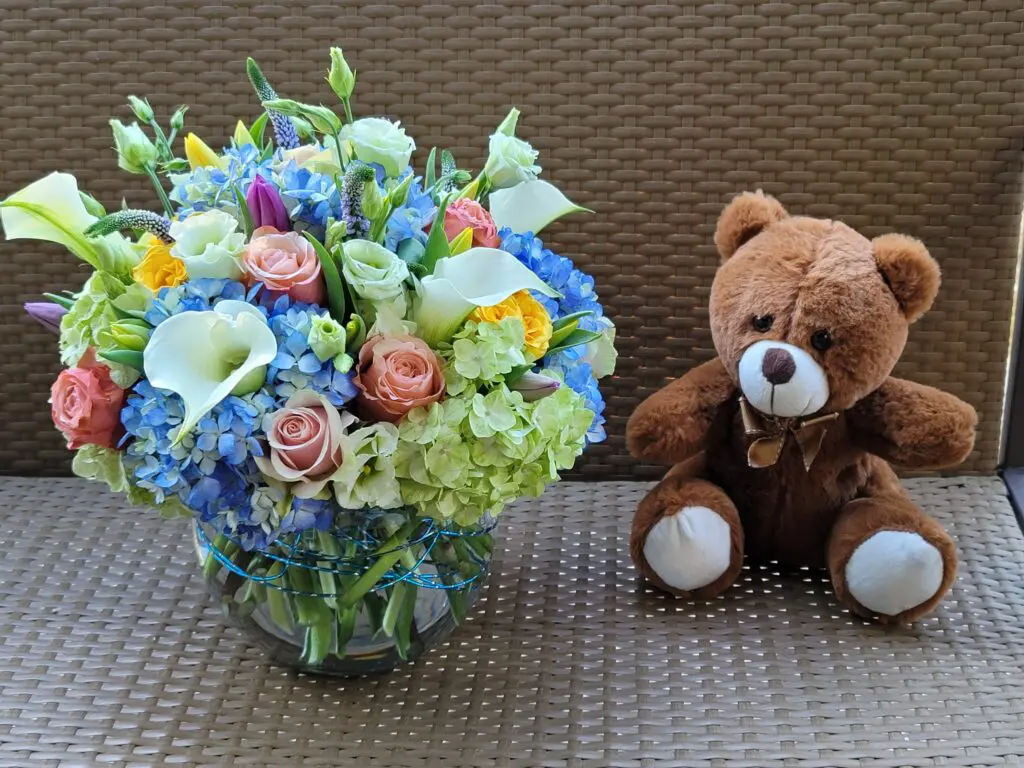 A teddy bear is sitting next to a vase of flowers