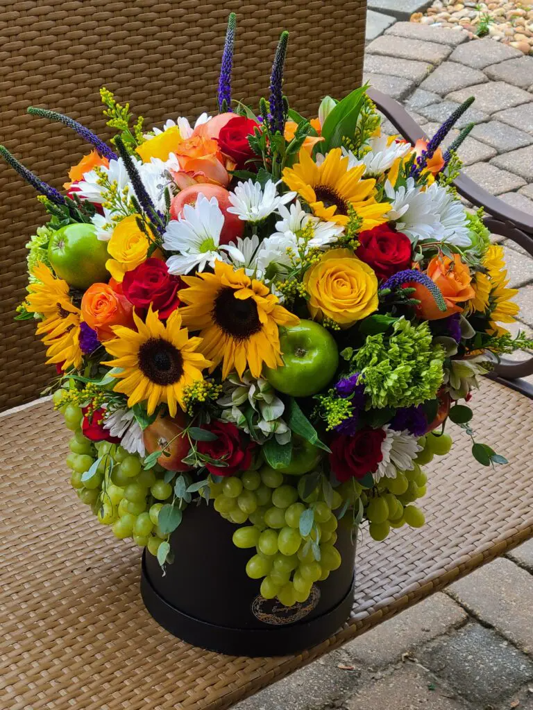 A vase filled with flowers and fruit is sitting on a table.