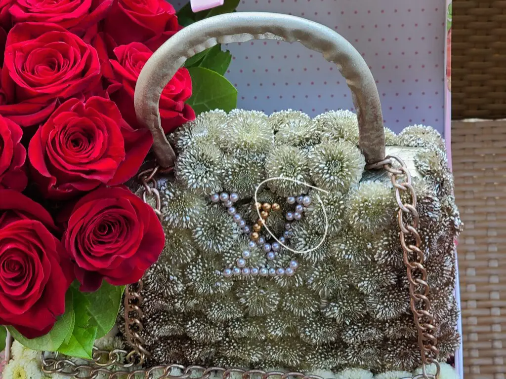 A purse made of flowers is sitting next to a bouquet of red roses.