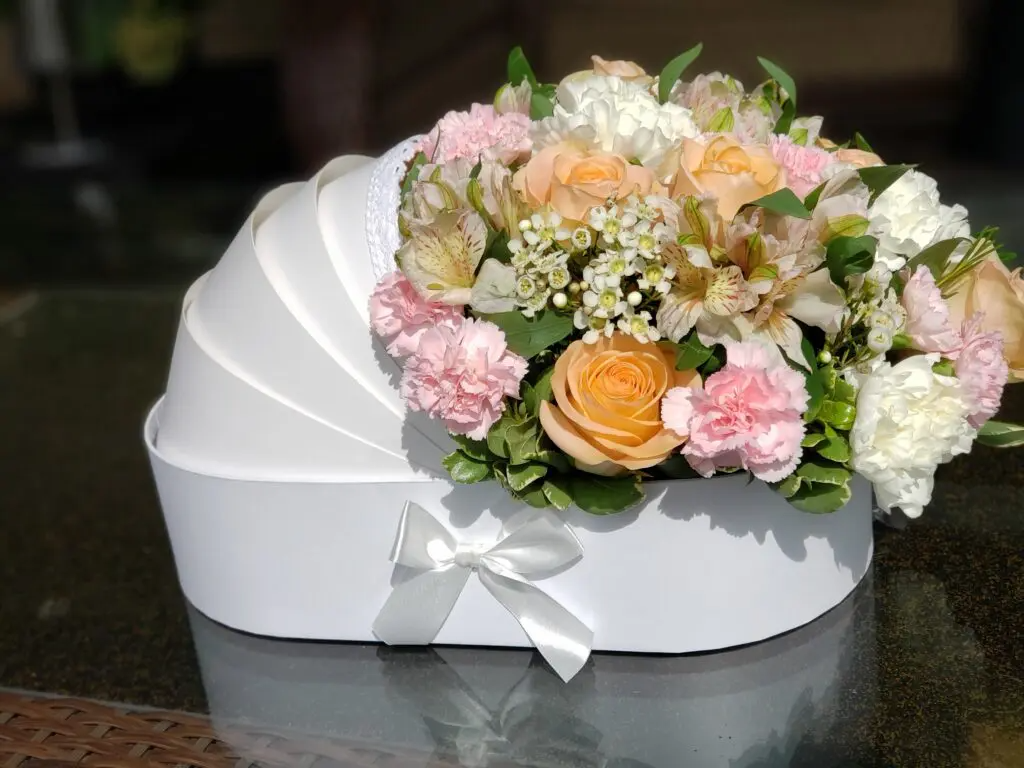 A white baby carriage filled with flowers is sitting on a table.