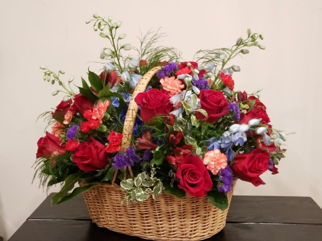 A wicker basket filled with red roses and blue carnations