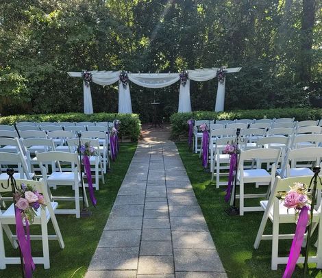 A row of white chairs are lined up on a brick walkway.