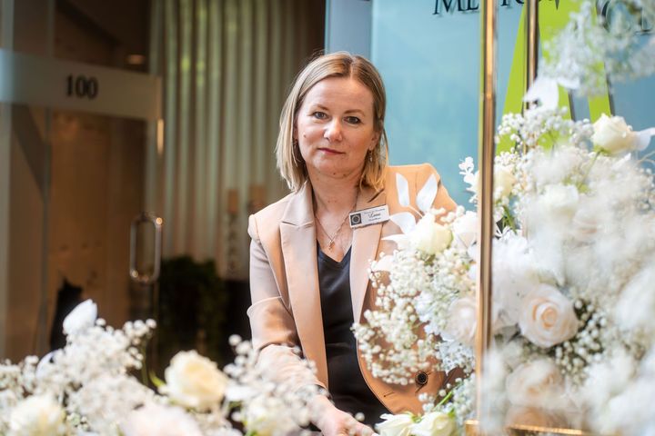 A woman is standing in front of a bunch of flowers in a room.