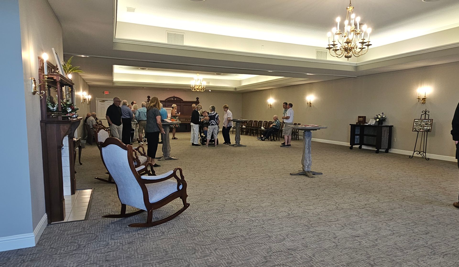 Spacious hotel lobby with a few people standing near the back and chandeliers overhead.