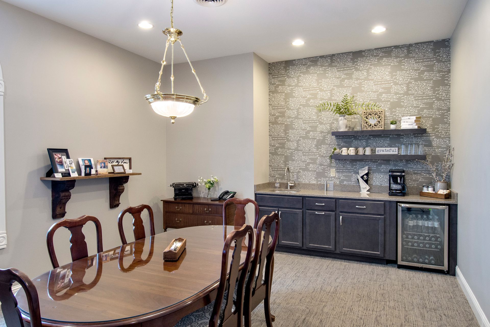 Elegant dining room with built-in bar, table set for six, overhead chandelier, and decorative shelf.