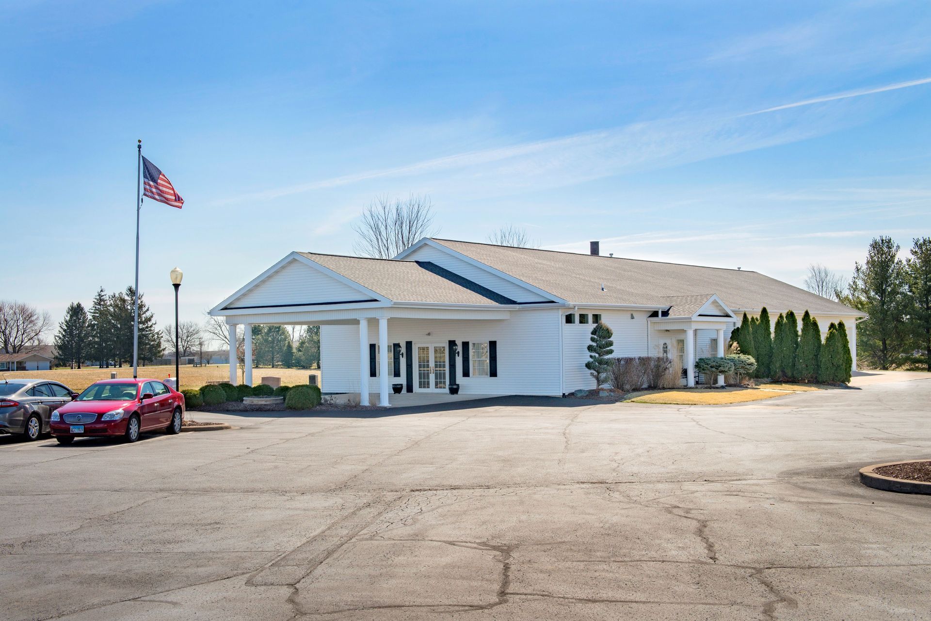 White building with American flag; cars parked in front, clear sky.