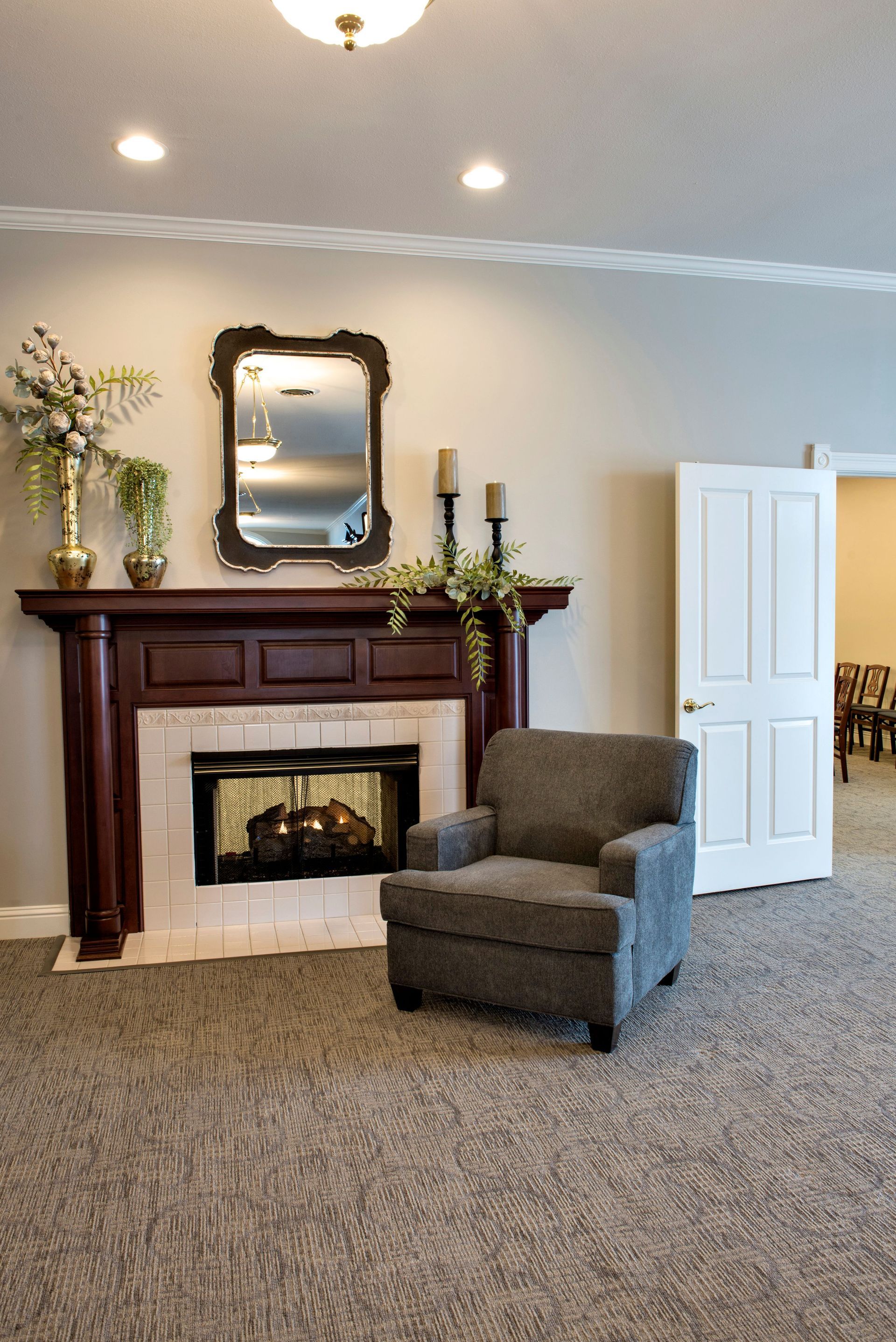 A cozy room with a fireplace, mirror, chair, and a door leading to another room.