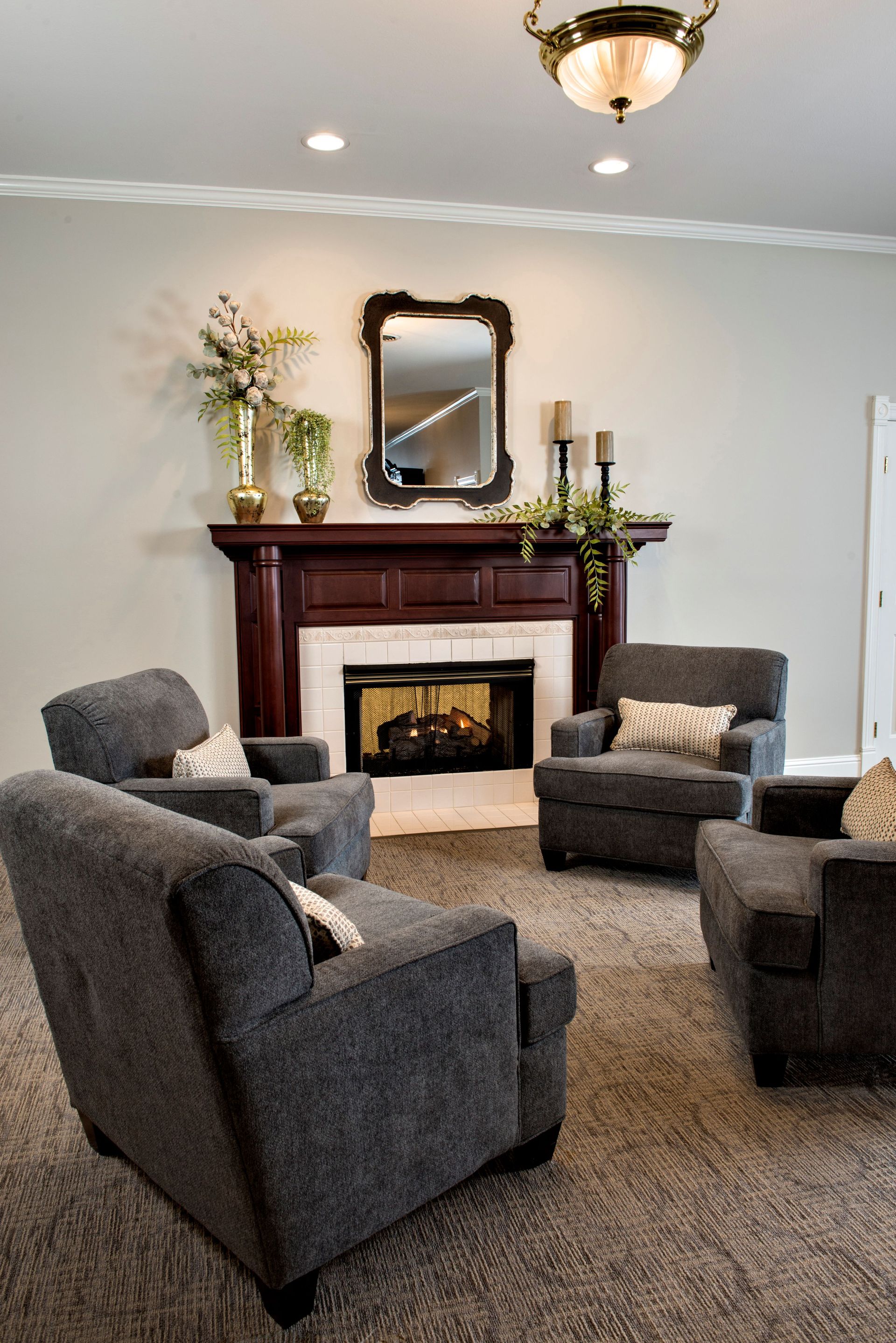 Living room with fireplace, four gray armchairs arranged for conversation, brown carpet.