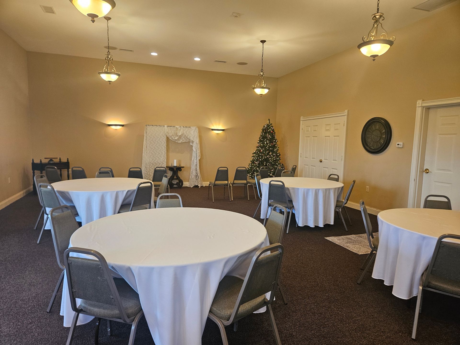 Empty banquet hall with round tables draped in white tablecloths and metal chairs