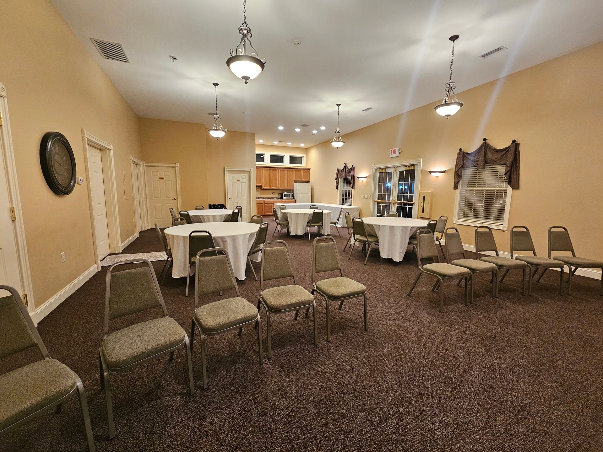 Empty banquet hall with round tables, chairs, pendant lights, and beige walls
