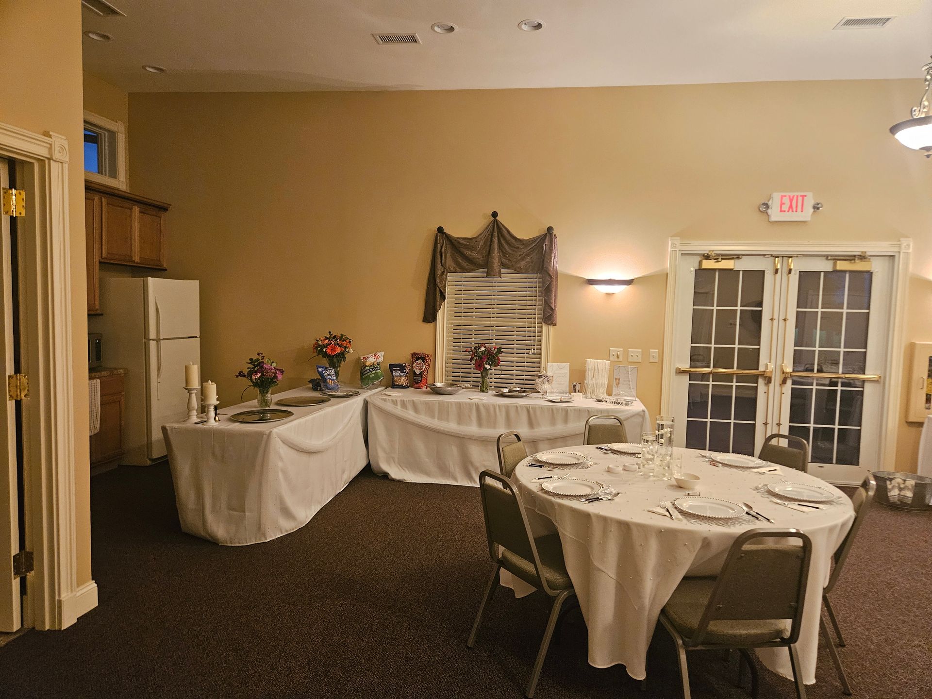 Banquet room with round tables, white tablecloths, and a serving table near double glass doors