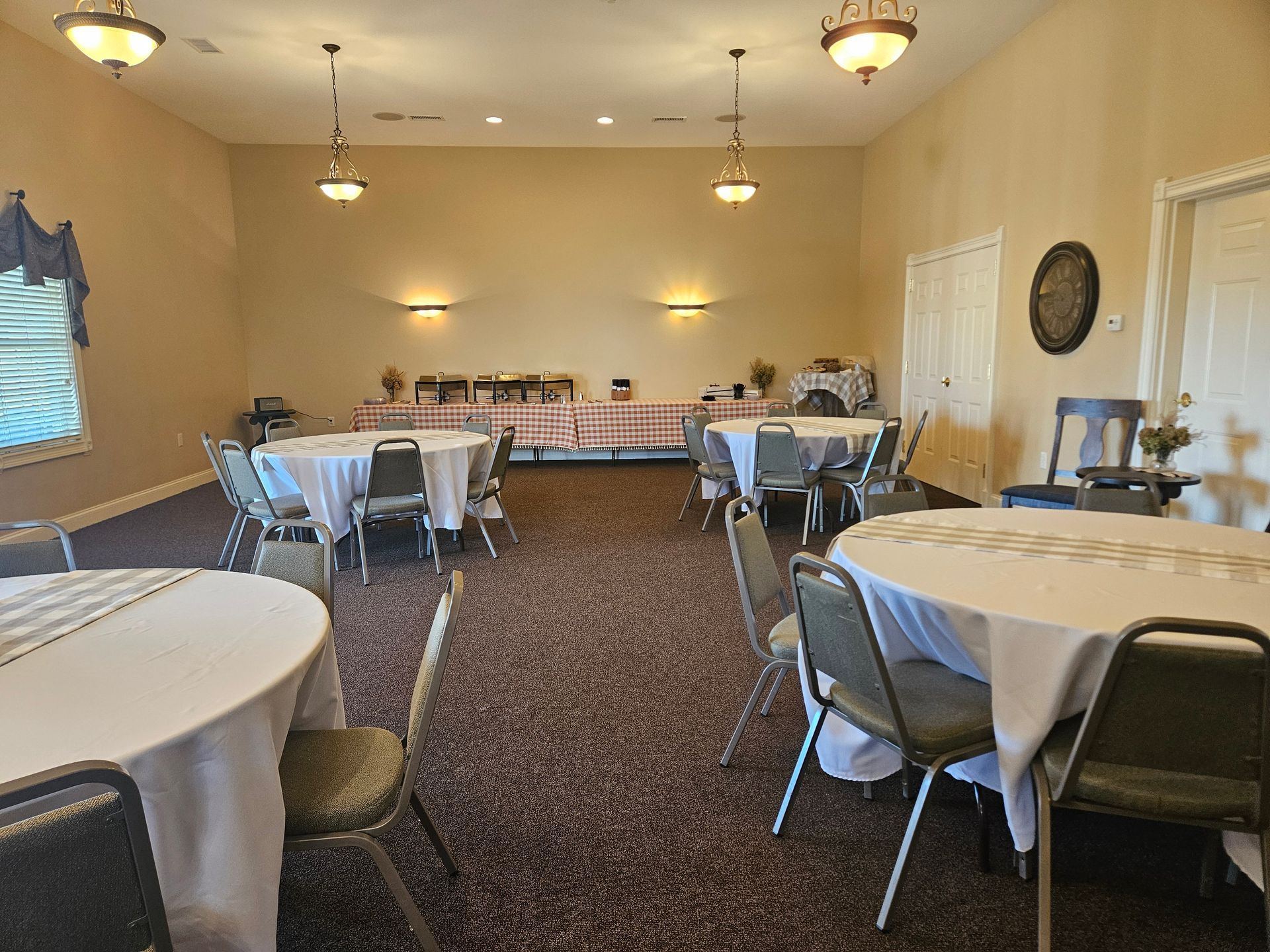 Empty banquet hall with round tables, white tablecloths, and folding chairs under warm ceiling lights