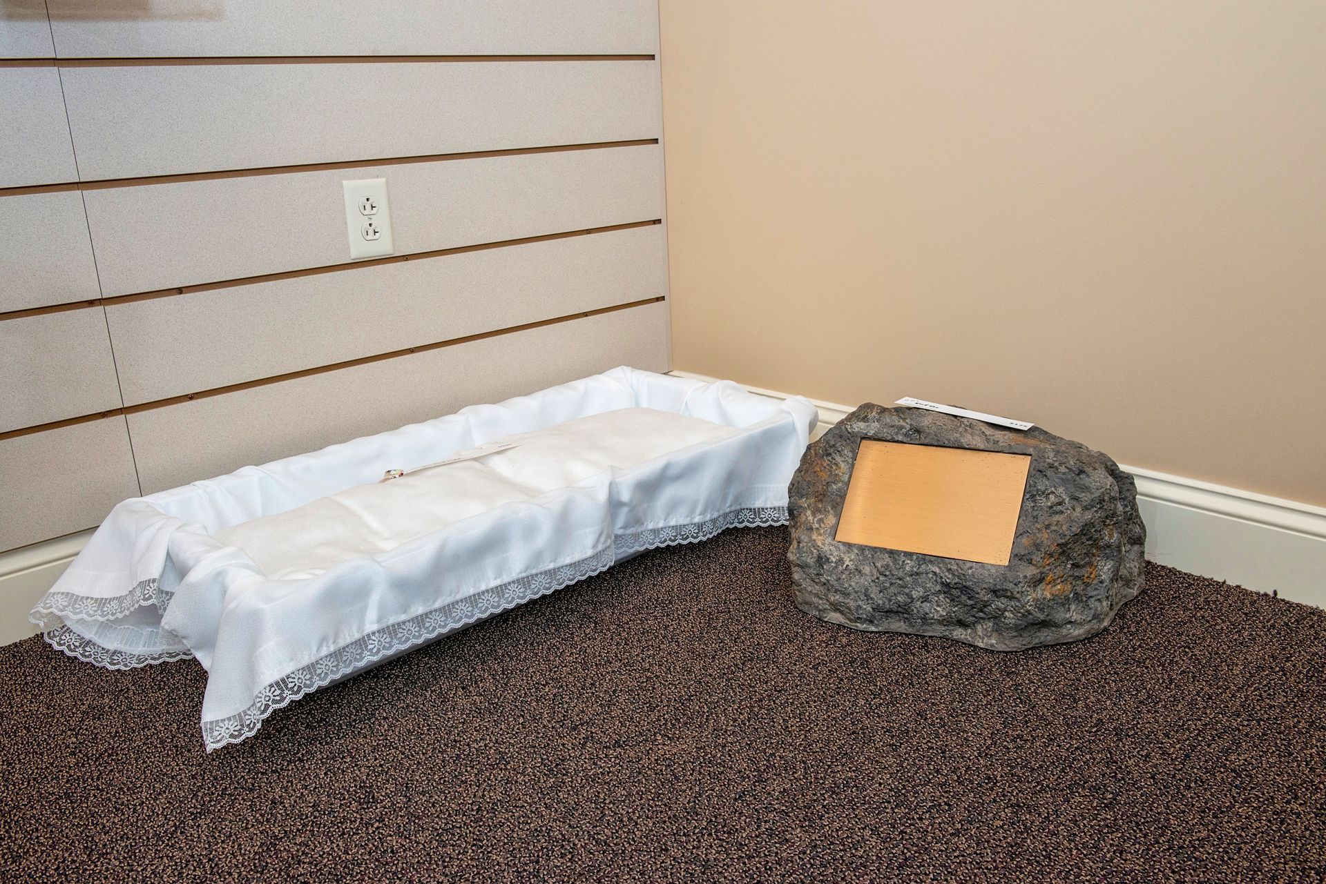 A white-draped, curved table next to a large rock with a copper plaque, in a room with a carpeted floor.