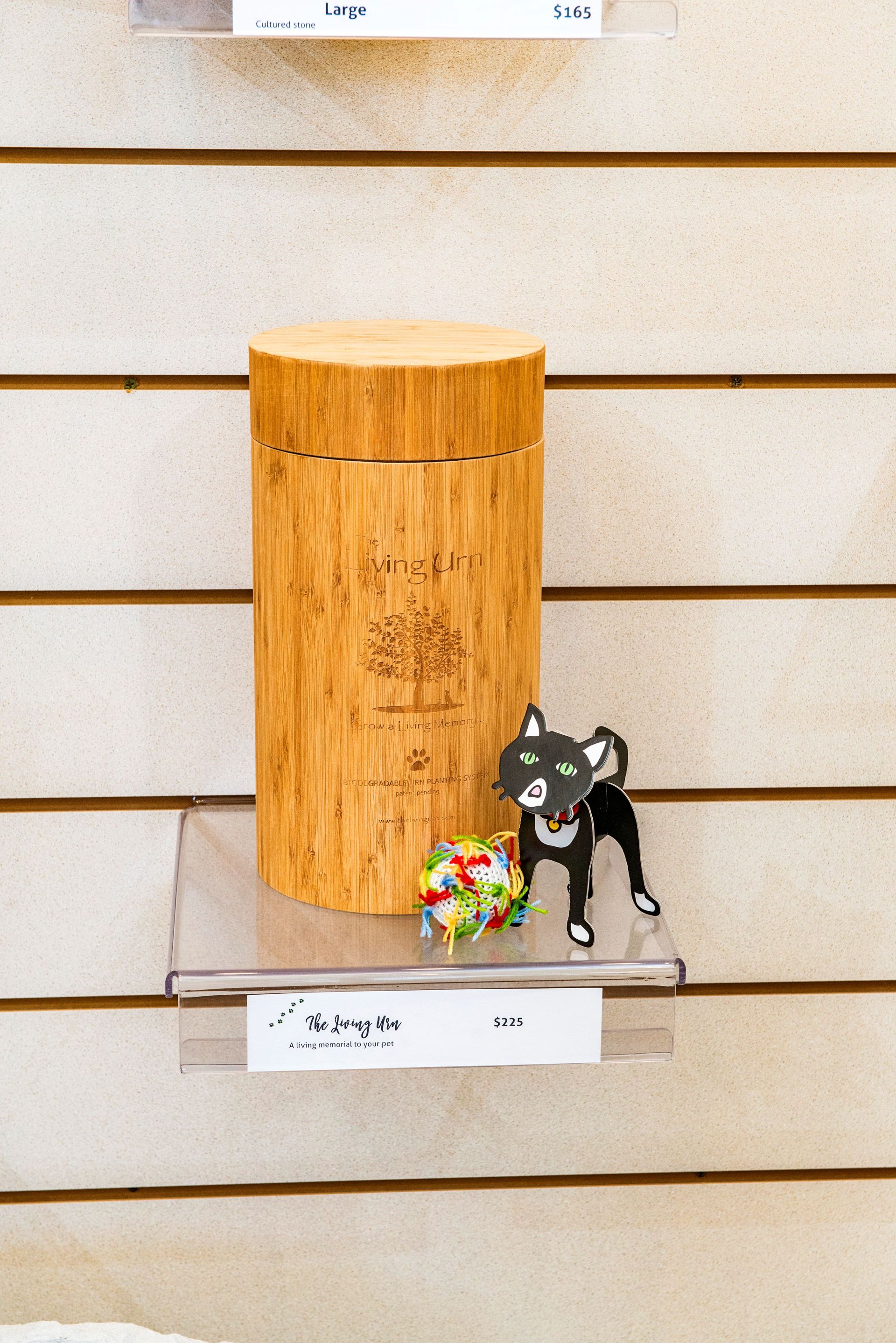 Wooden pet urn with black cat figurine and colorful ball on shelf.