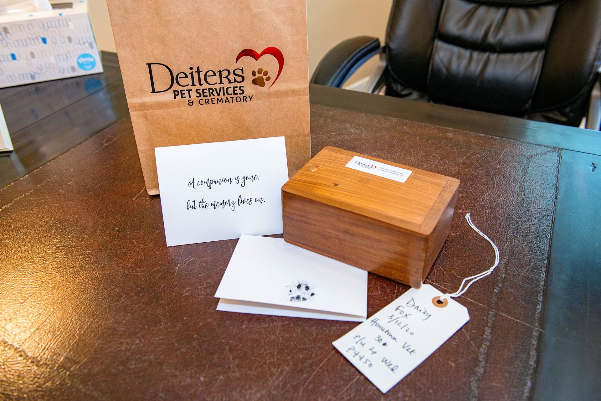 Brown paper bag, wooden box, and cards on a desk with the Deiters Pet Services logo.