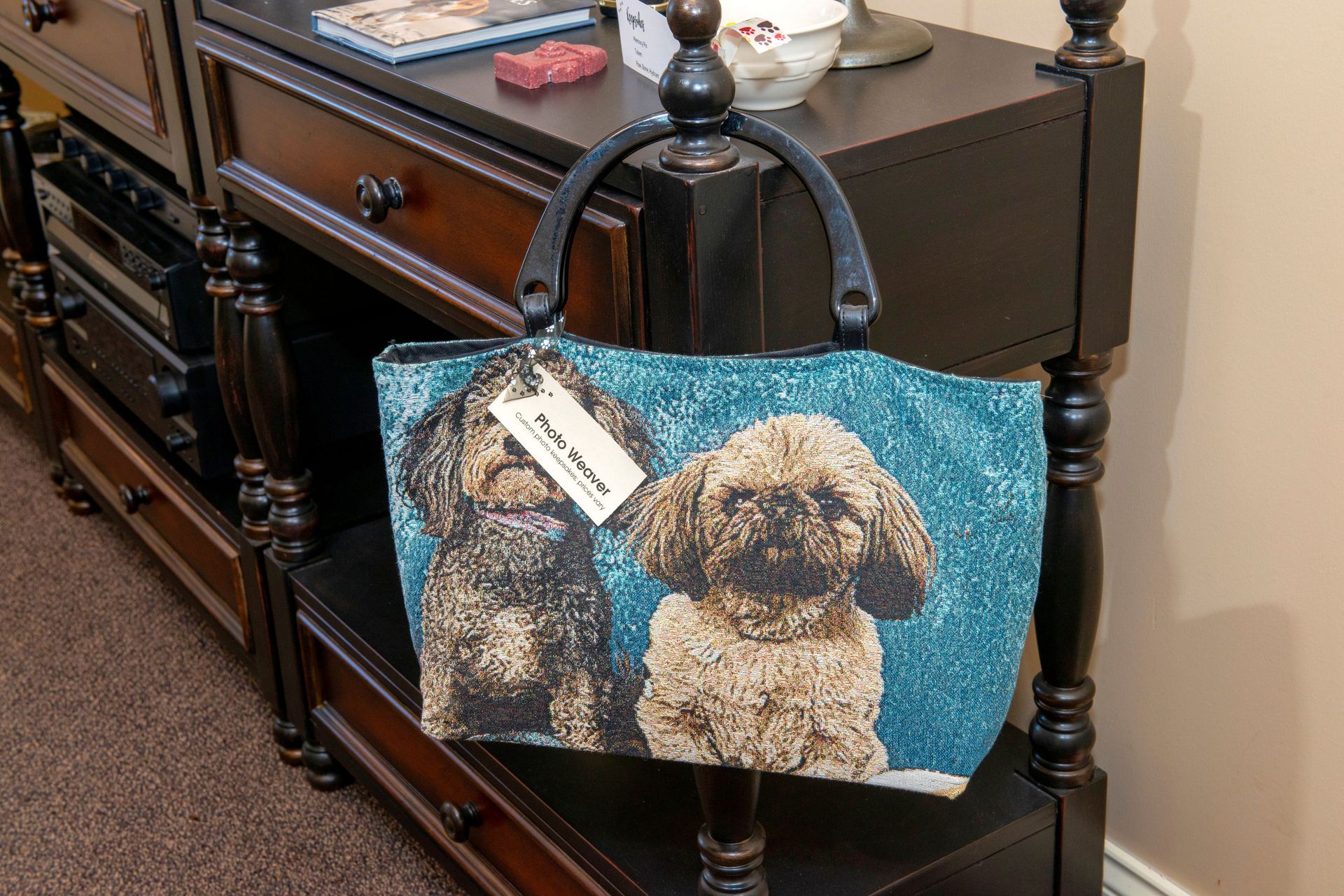 Dog-themed tote bag on a black, ornate shelf. The bag features two poodle portraits against a blue background.