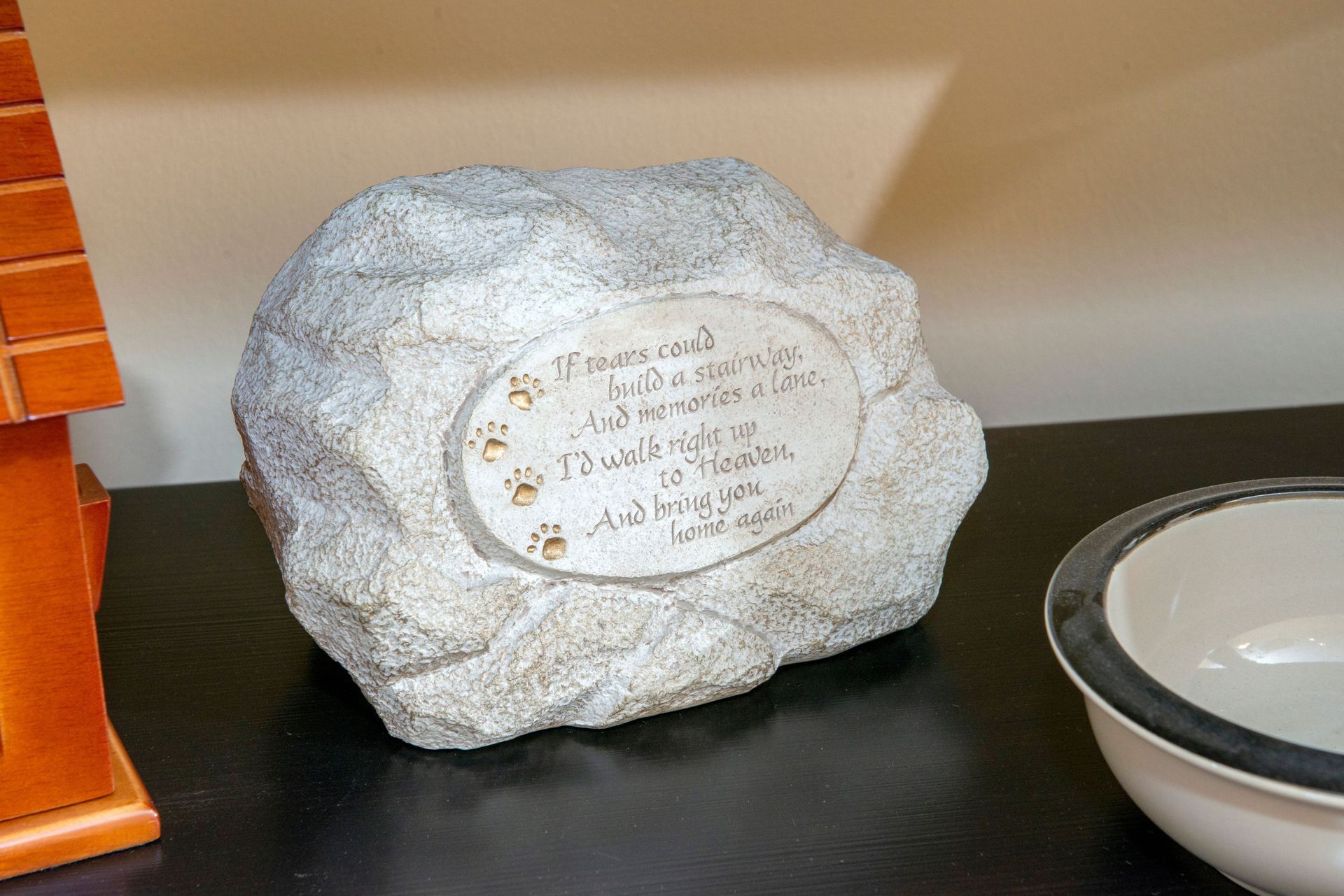 Stone pet memorial with inscription and paw prints, on a shelf next to a bowl.