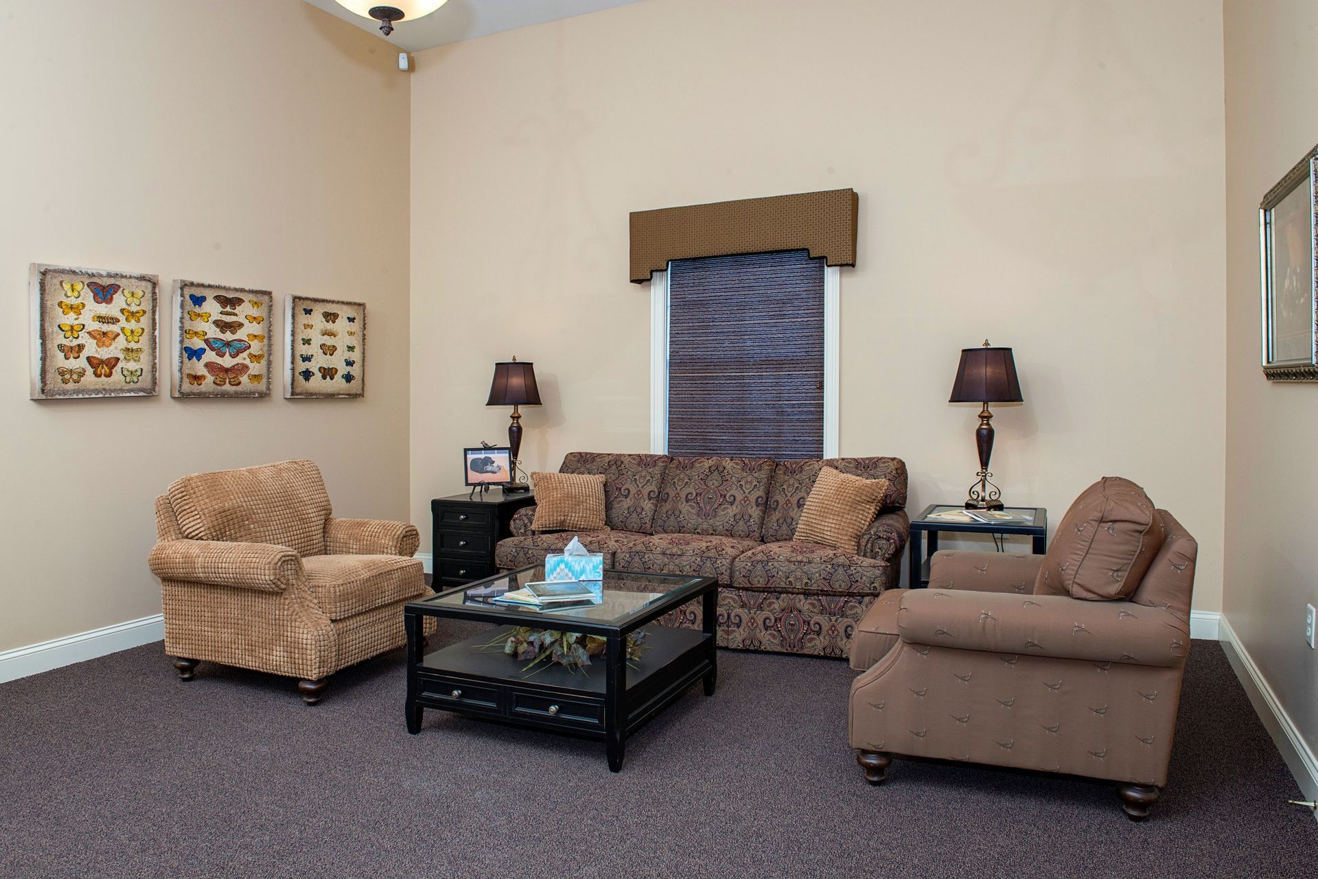 Cozy living room with beige walls, brown patterned sofa, two armchairs, coffee table, lamps, and artwork.