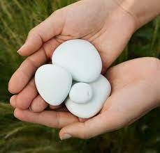 Hands holding a cluster of four smooth, white stones against a blurry green background.