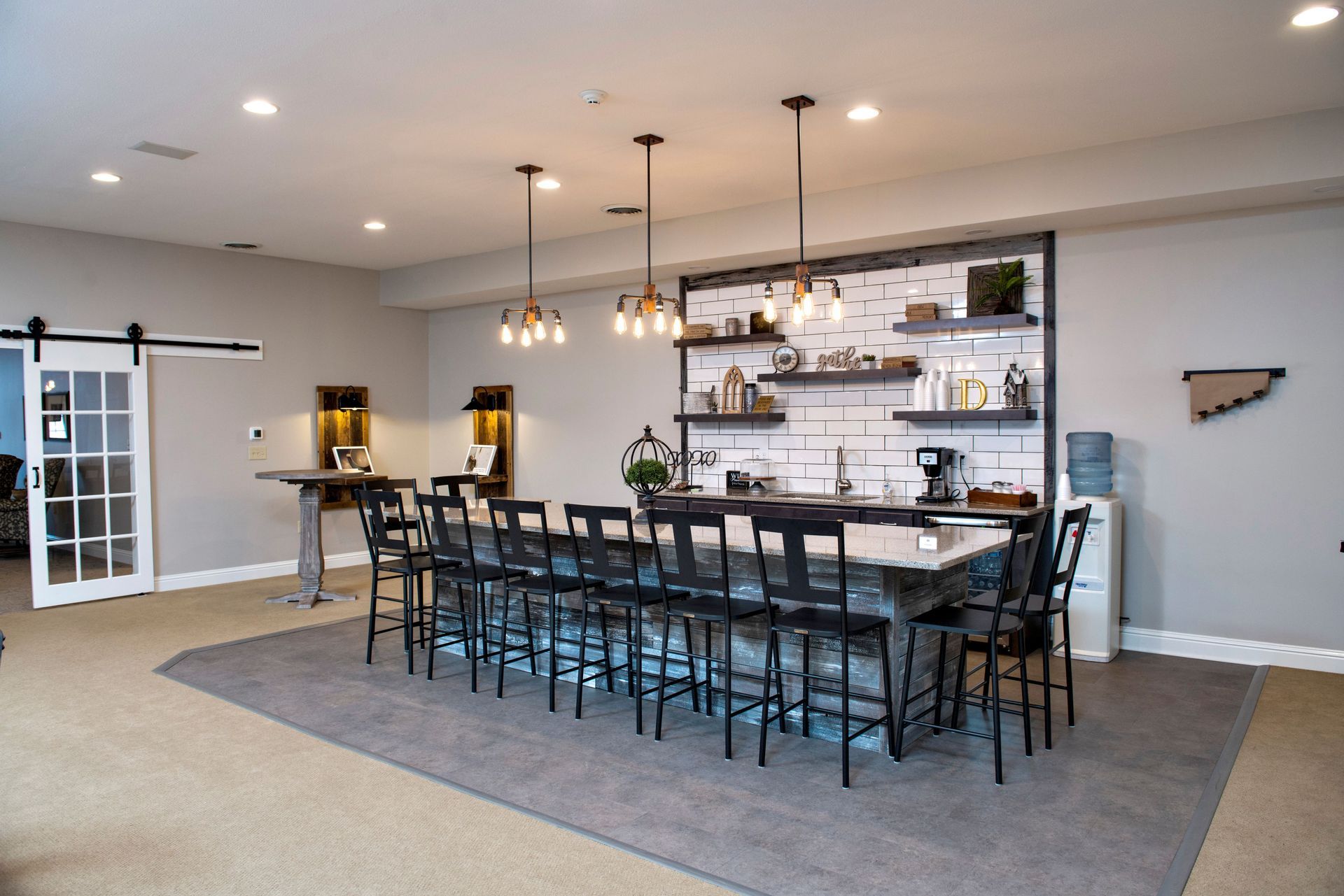 Large modern bar with stools, pendant lights, and shelving, in a room with a sliding door and grey carpet.