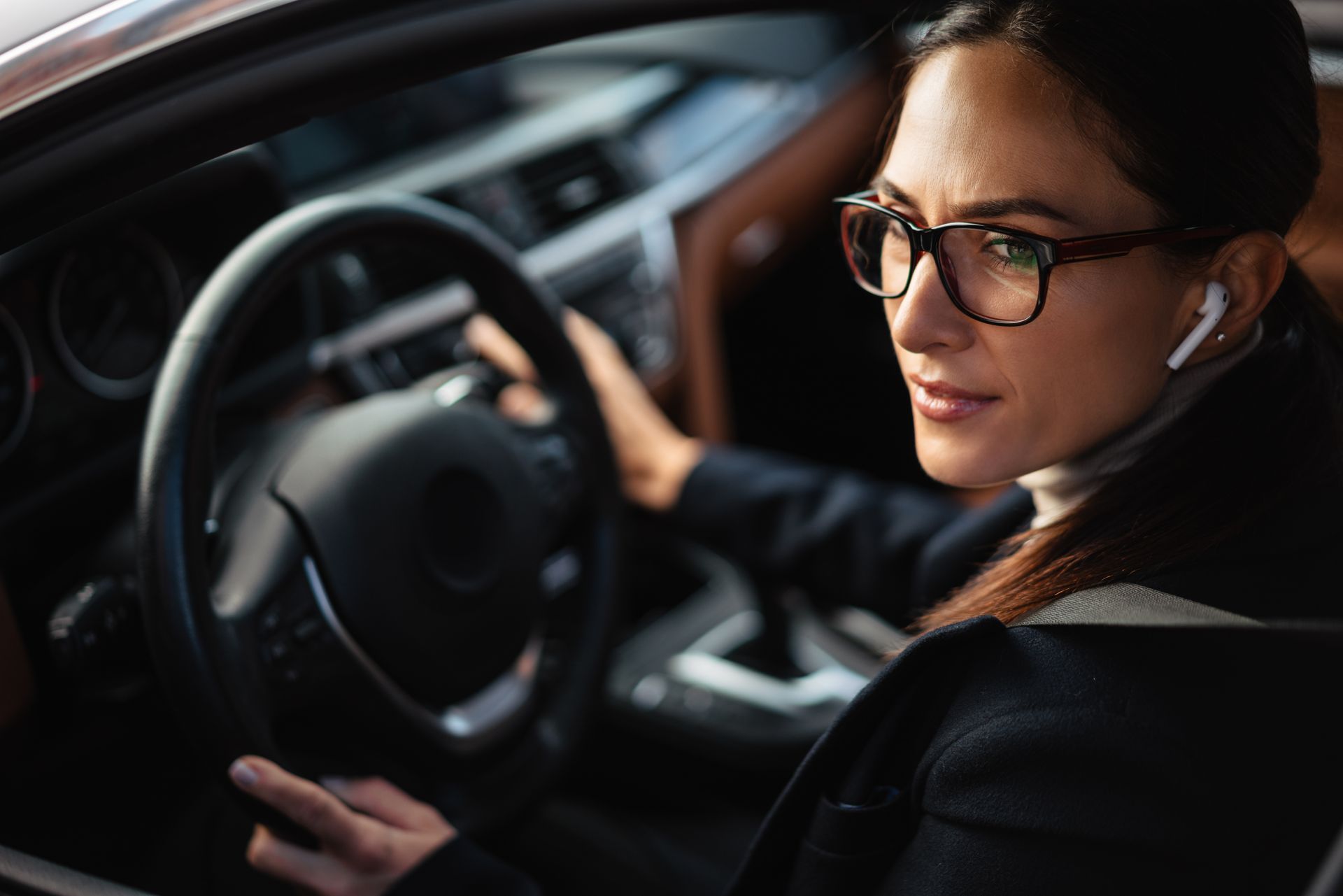 Frau mit Brille fährt Auto, blickt mit den Händen am Lenkrad in die Kamera.