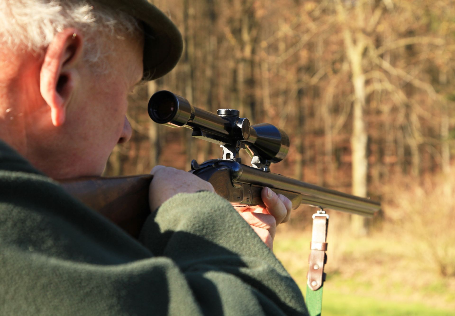 Eine Person zielt mit einem Gewehr mit Zielfernrohr auf einem freien Feld, von hinten gesehen.