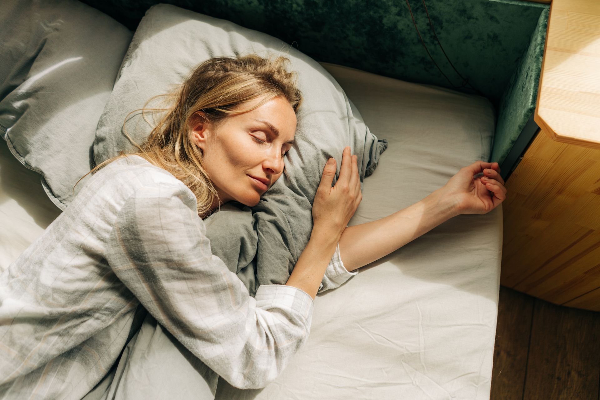 Frau schläft auf einem Bett mit weißen Laken, den Arm neben sich ausgestreckt.