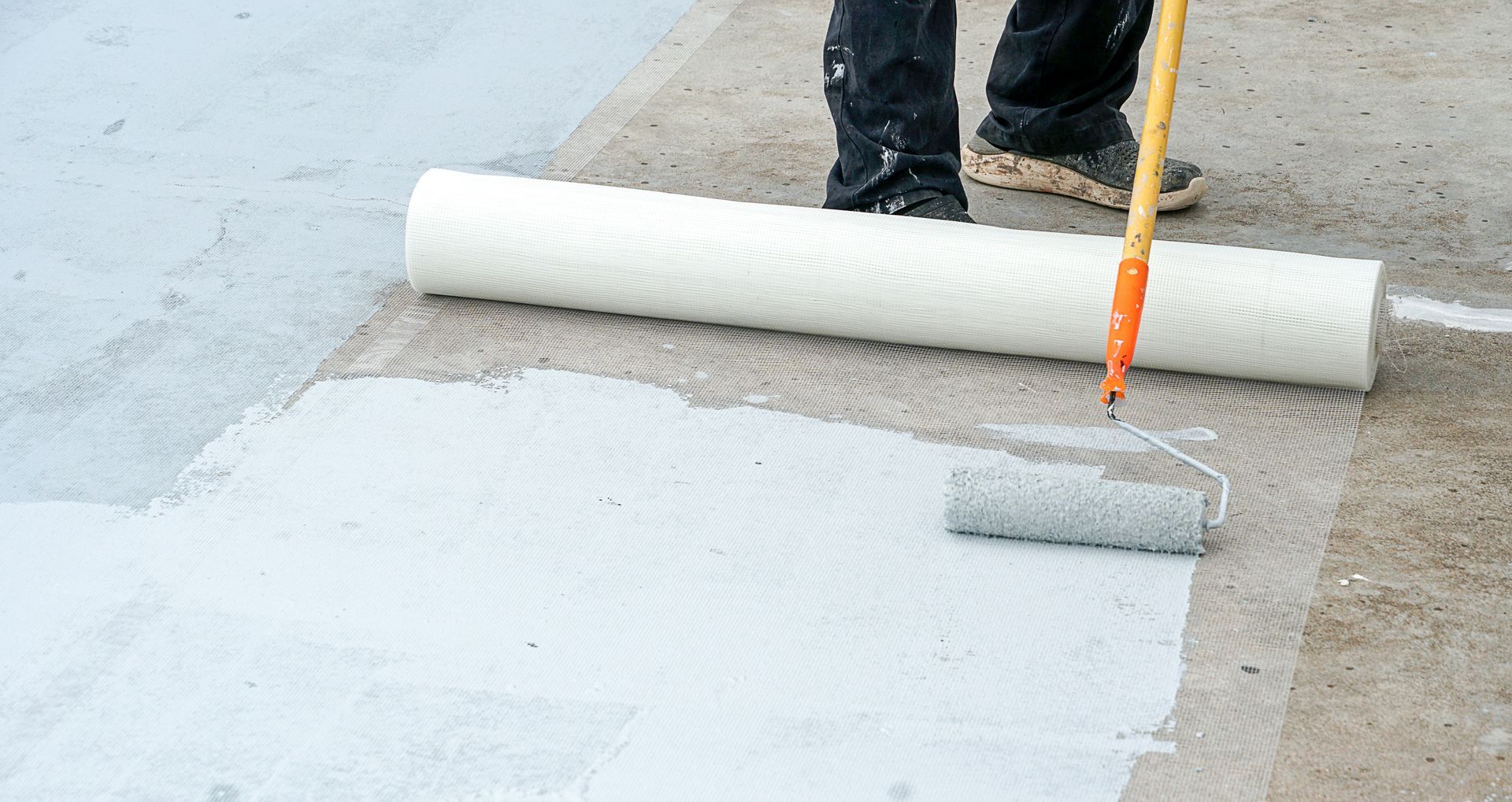 a man is painting a concrete surface with a roller .