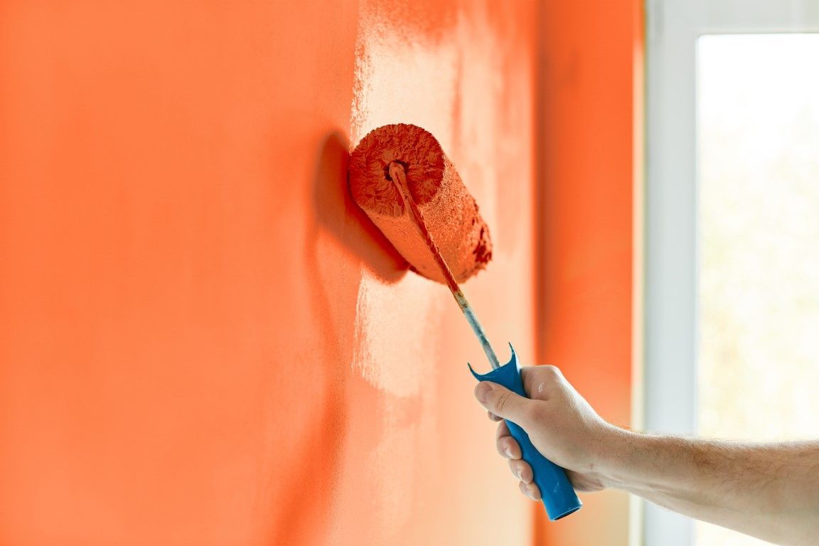 up close picture of a paint roller painting a wall orange