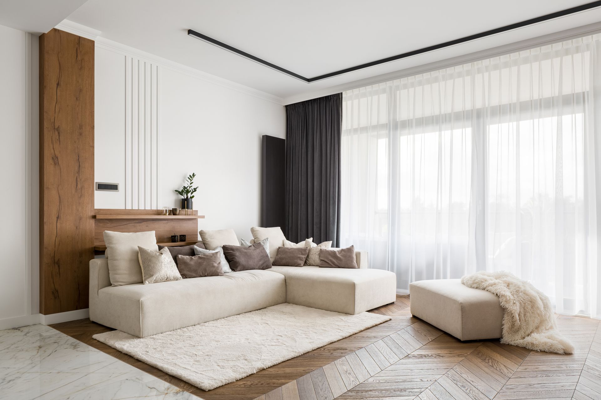 Bright modern bedroom with a large bed, sheer curtains, and sunlight streaming across the carpet.