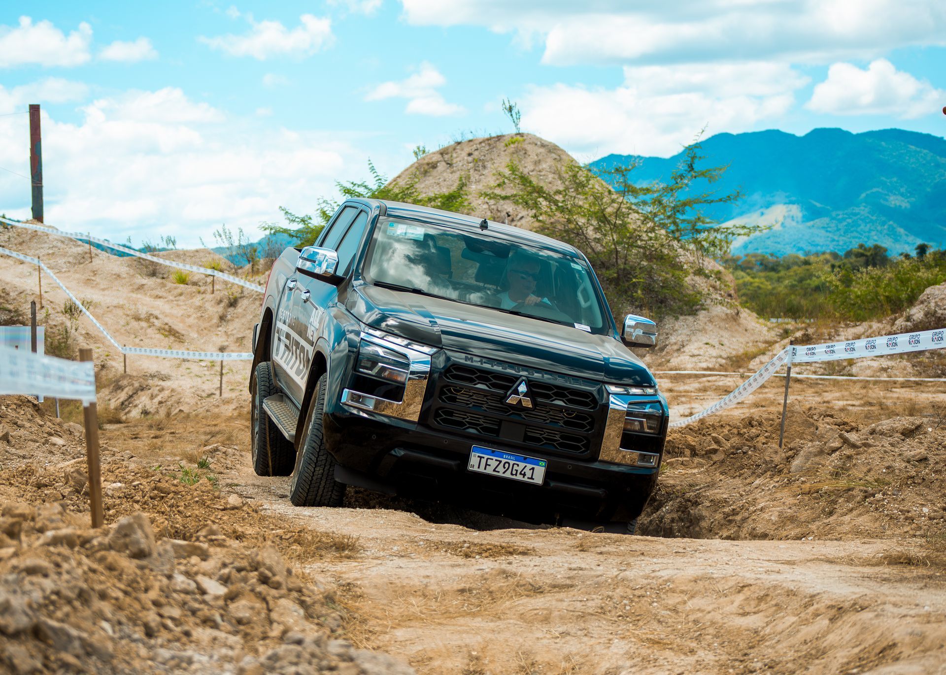 Uma caminhonete Mitsubishi preta trafegando em um terreno acidentado, em uma estrada de terra