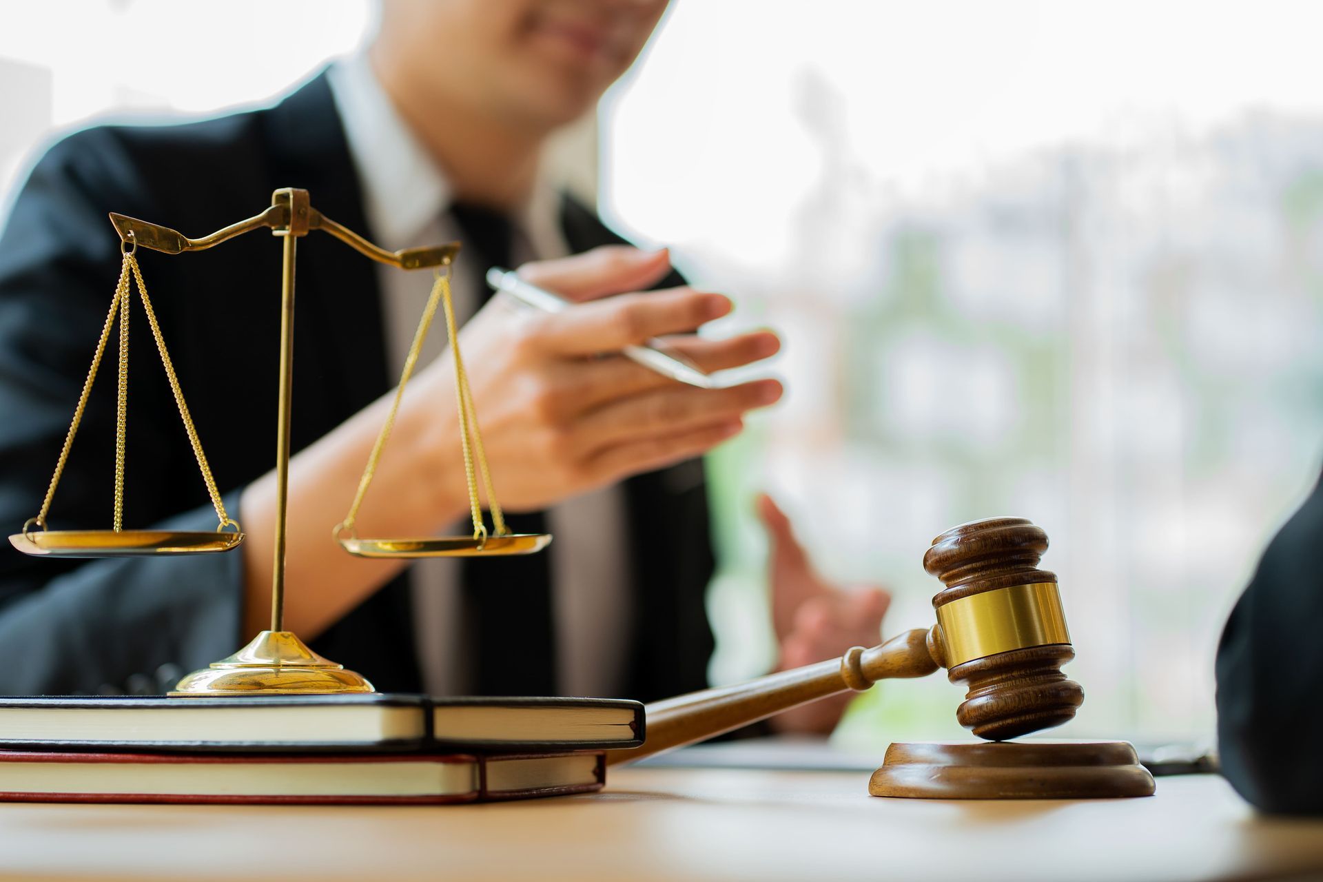 Scales of justice and gavel on a desk with a blurred lawyer in the background.