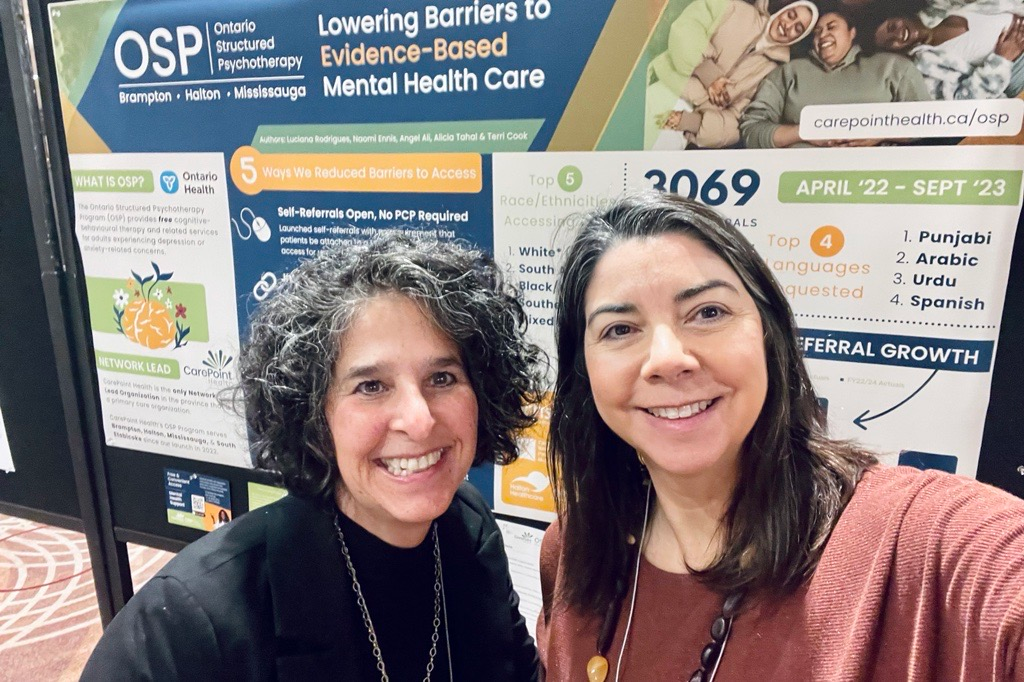 two women standing in front of a sign that says lowering barriers to evidence-based mental health care