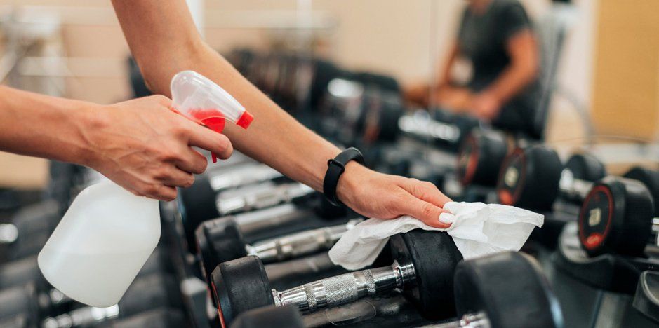 A gym-goer spraying disinfectant on gym equipment