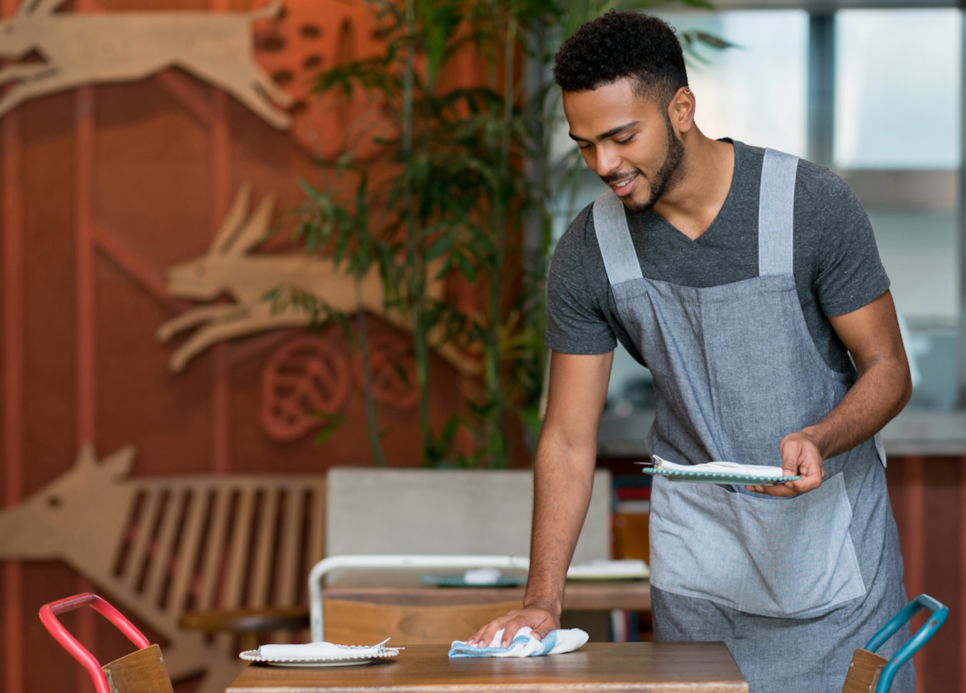 Young waiter cleaning a restaurant table while holding a plate