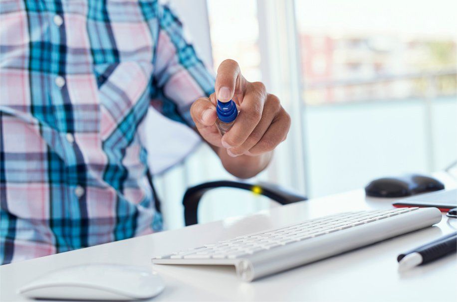 Diligent employee disinfecting work desk with antibacterial spray