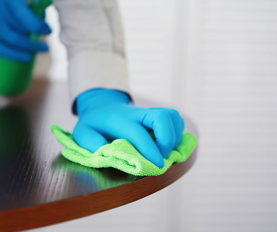 A janitorial cleaning team member dusting and cleaning a table top.