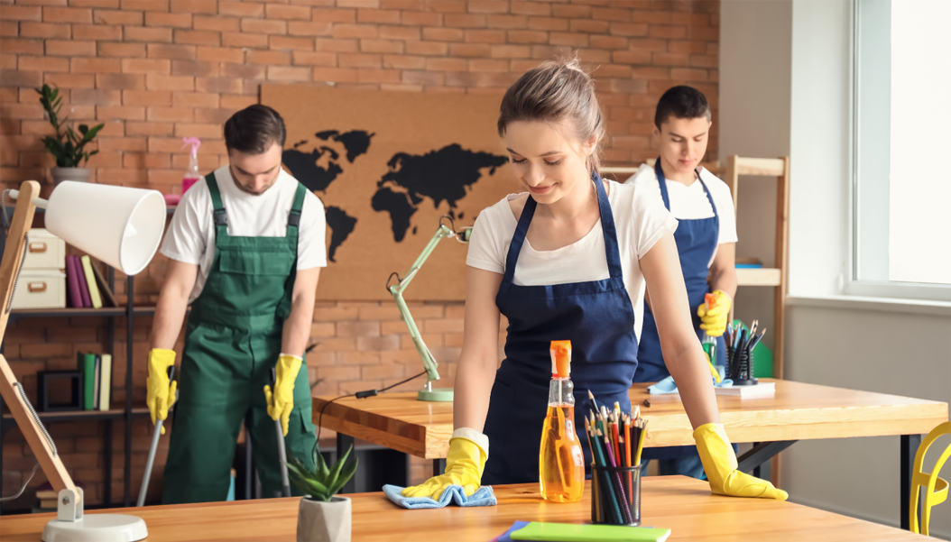 Professional office cleaners spraying and wiping desks and sweeping floors