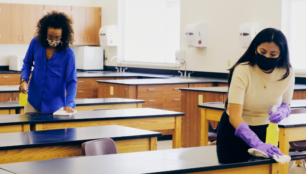 two women cleaning the classroom while wearing masks