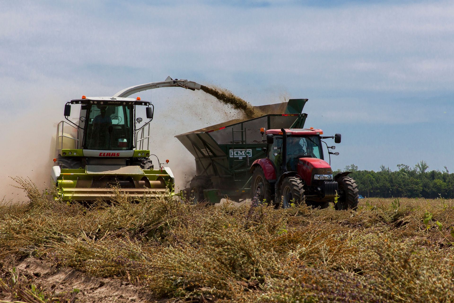 a combine delivering it's payload into another tractor on a farm