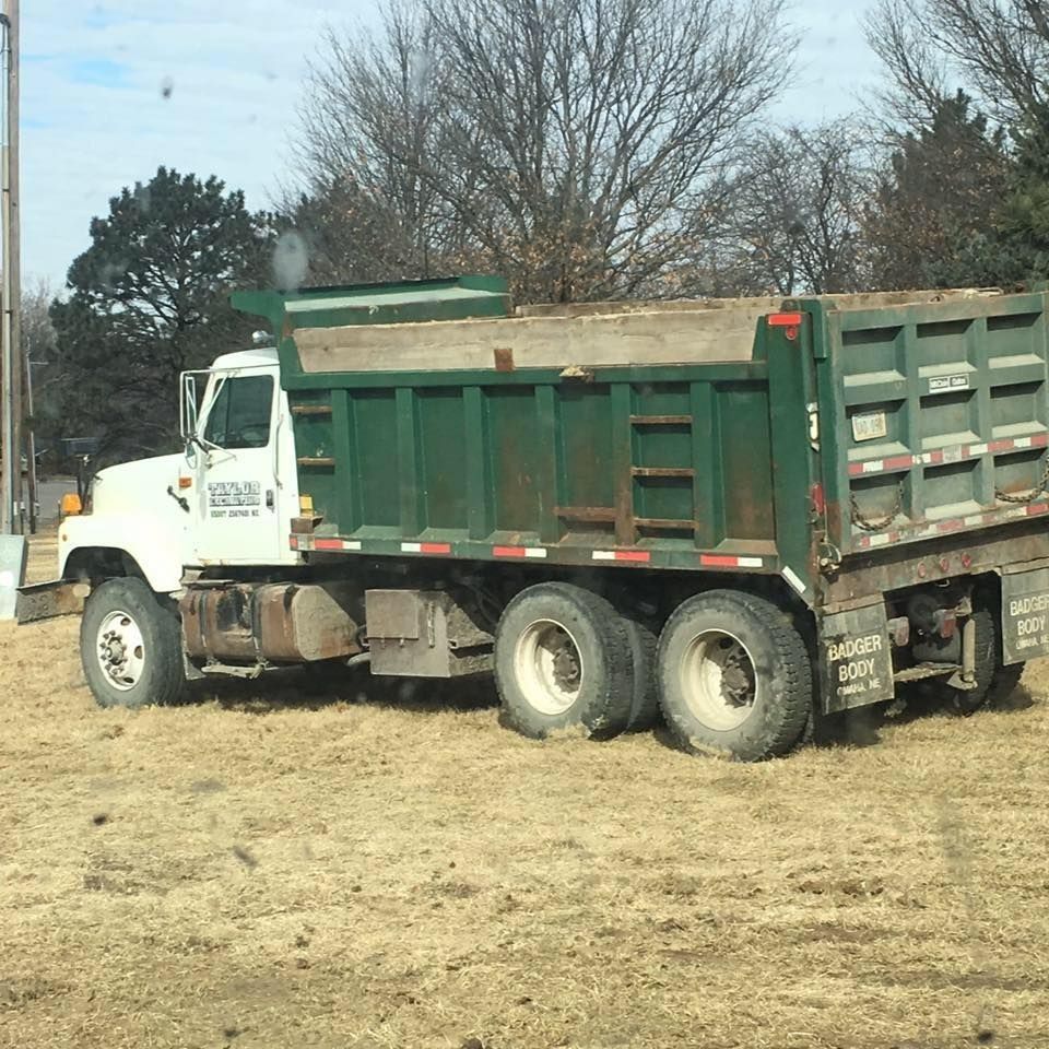 White dump truck with green trailer parked on dry grass beside trees