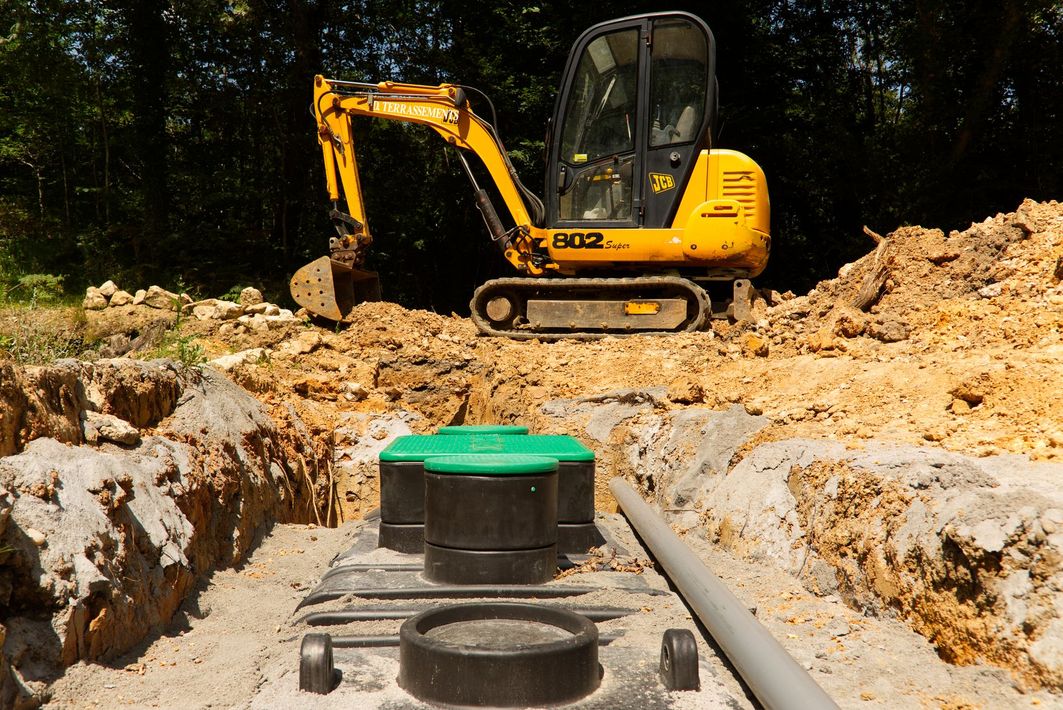 Yellow excavator at a trench with pipes and a green utility box in the foreground