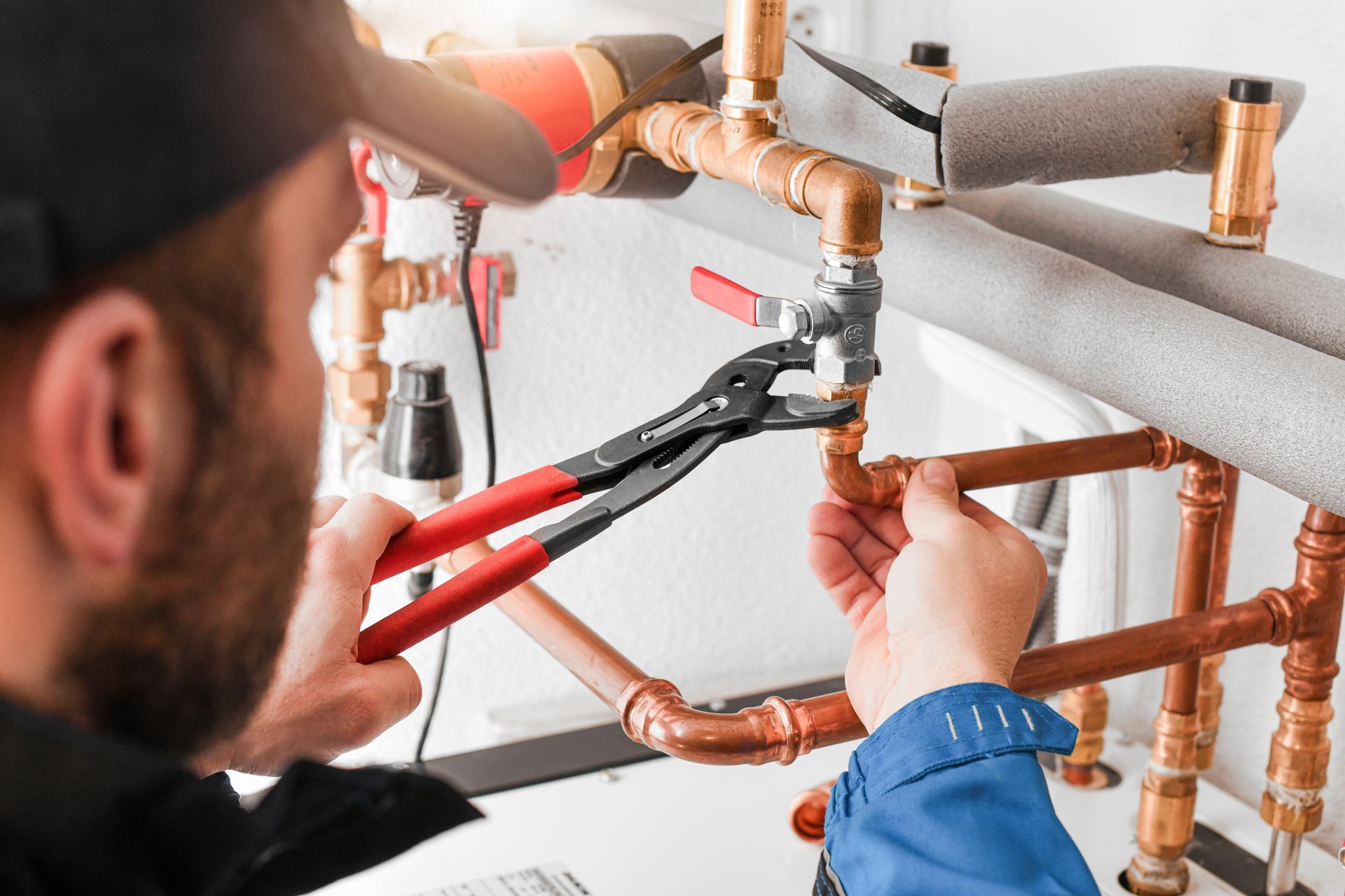 Worker tightening copper plumbing pipes with red pliers inside a wall cavity
