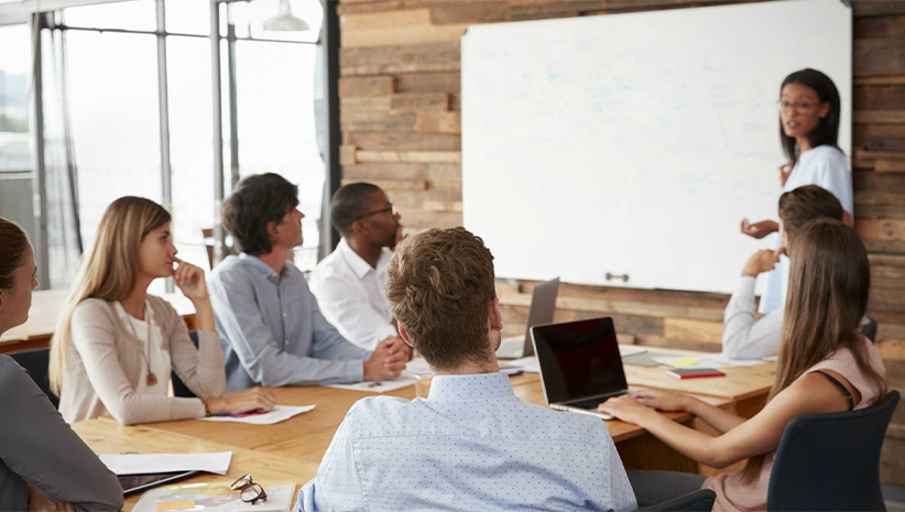 A group of people are sitting around a table listening to a presentation.