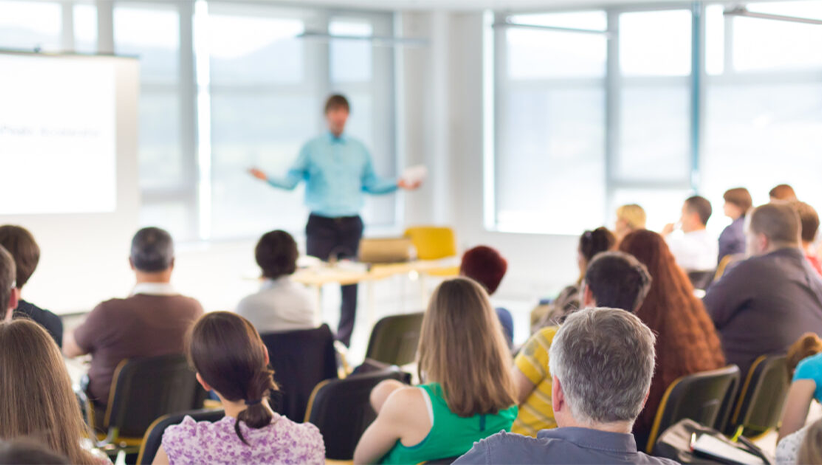 A group of people are sitting in chairs in front of a man giving a presentation.