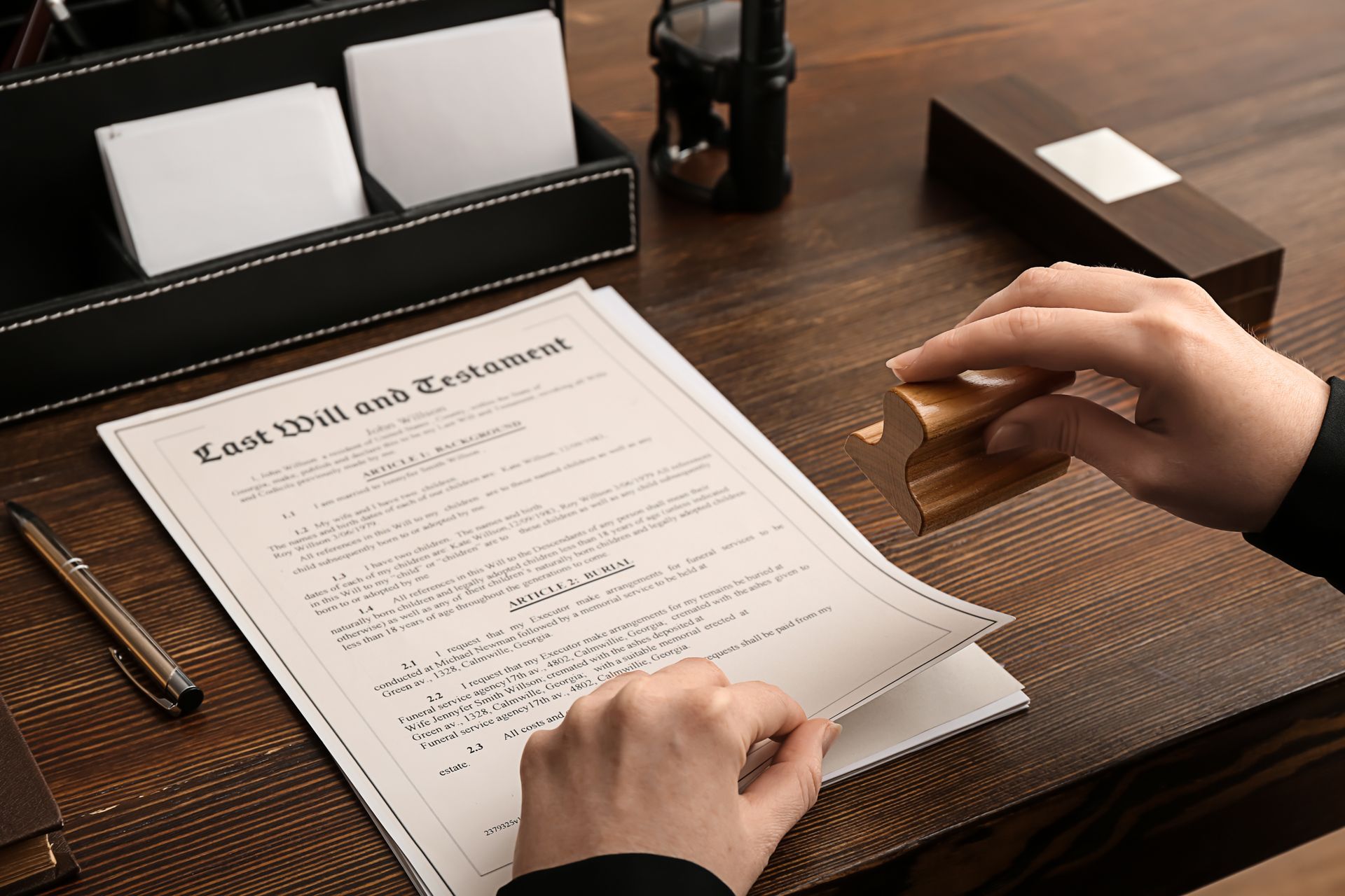 Hands filling out a legal form on a desk with organized office supplies and a pen holder