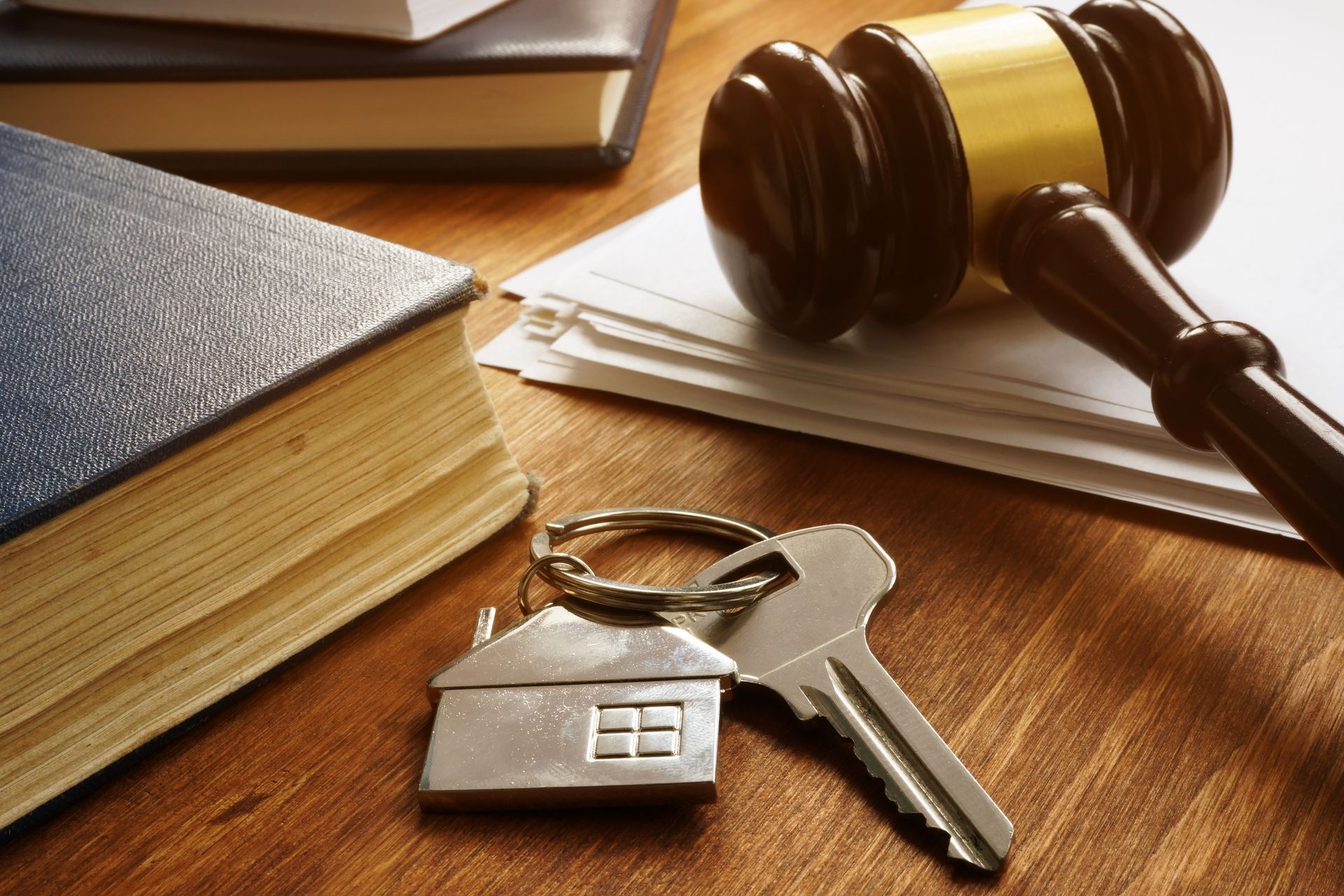 Judge's gavel, house key, and keychain on a wooden desk beside legal books and papers.